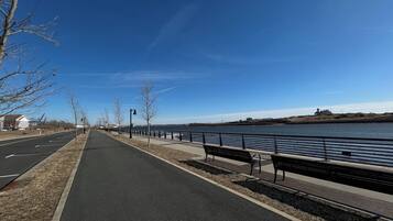 A riverside walkway with benches, a bike lane, and a fence along the water.