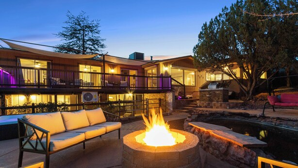 A cozy outdoor seating area with a fire pit, a pool, and a well-lit building with multiple balconies. - Experience luxury at the Sedona House of Wren & Koi, a spacious 5-bedroom retreat! (Sedona)
