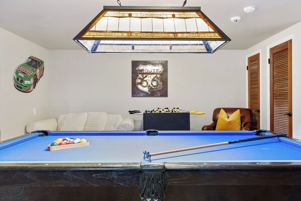 A pool table with a blue felt surface, a pool cue, and a set of balls. There is a framed Route 66 sign above the table.