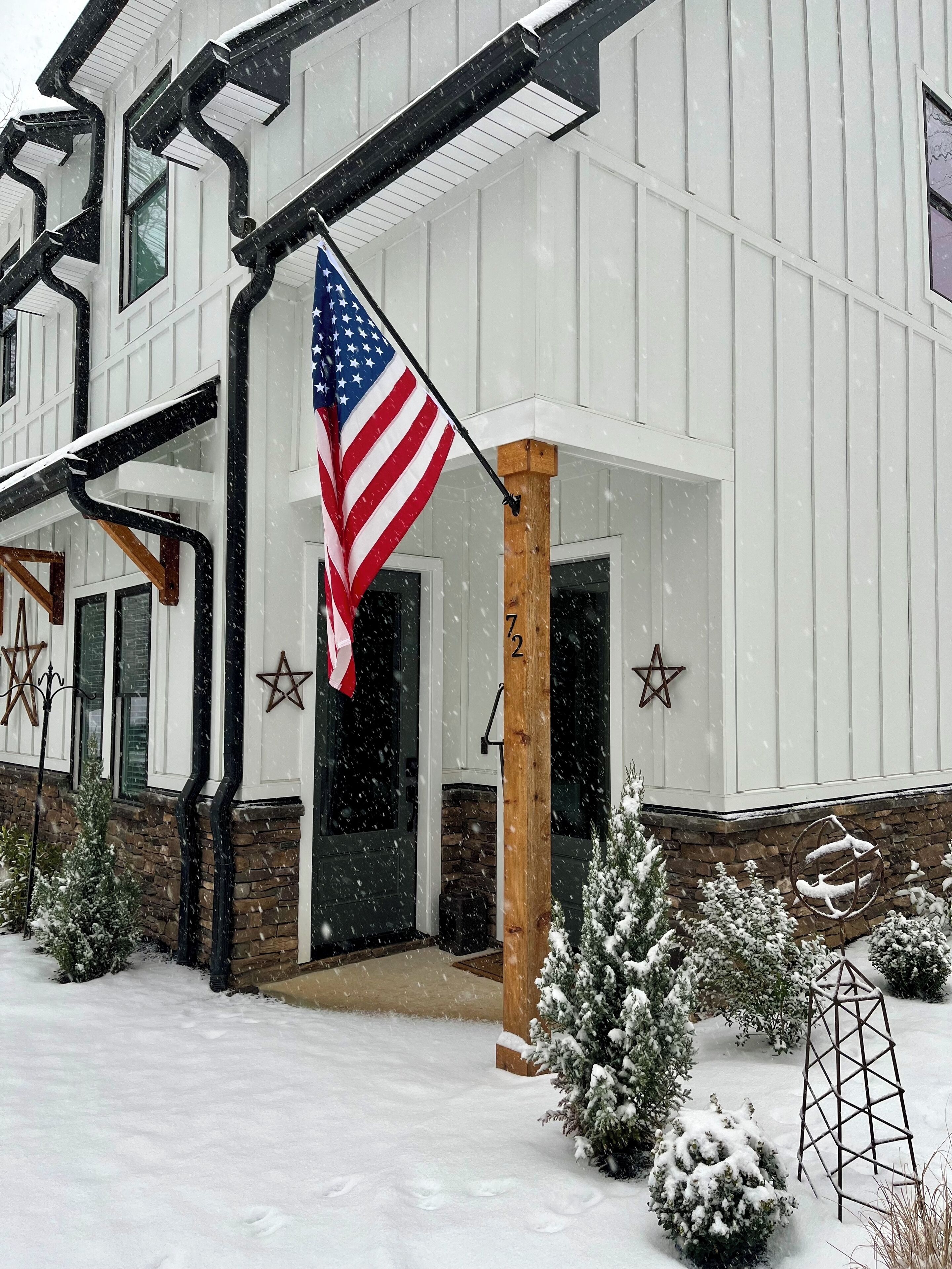 A snow-covered house with an American flag, a Star of David, and a Star of David on the porch.