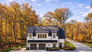 A two-story house with a garage, surrounded by a driveway, and set in a forest with autumn foliage.