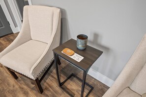 Un sillón color crema, una mesita de madera con un posavasos y una tarjeta de bienvenida, y una taza de cerámica sobre la mesa.