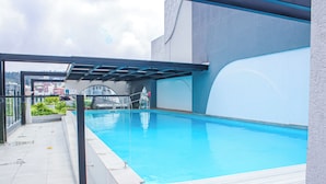 Piscina interna com estrutura de vidro, deck revestido com azulejos e vista para o horizonte da cidade ao fundo.