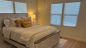 A bedroom with a wooden bed frame, a patterned rug, and a nightstand with a lamp. - Cozy Ranch House (Fredonia)