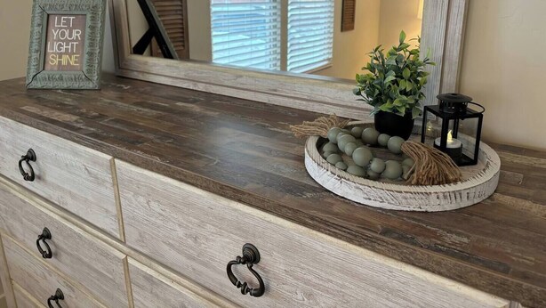 A wooden dresser with a mirror, a framed inspirational quote, a potted plant, and a lantern. - Cozy Ranch House (Fredonia)