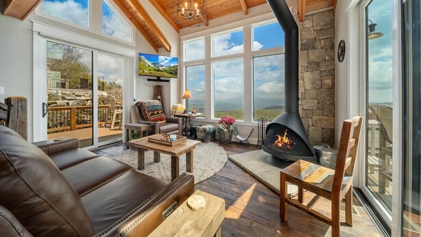 Una sala de estar acogedora con chimenea, sofá de cuero, mesa de centro de madera y grandes ventanales que ofrecen vistas panorámicas.