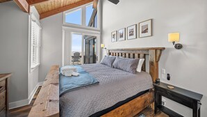 Un dormitorio con cama de madera, ventilador de techo, banca y vistas al exterior.