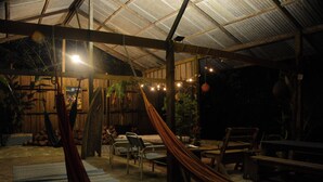 Un espacio al aire libre rústico con una hamaca, muebles de madera y luces colgantes.