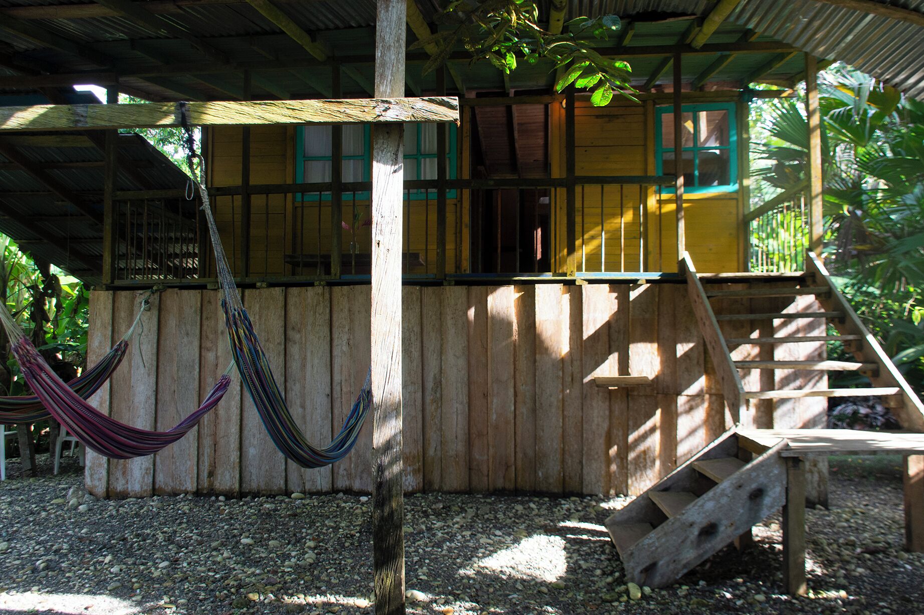 A wooden structure with a staircase leading to a yellow door, surrounded by greenery.