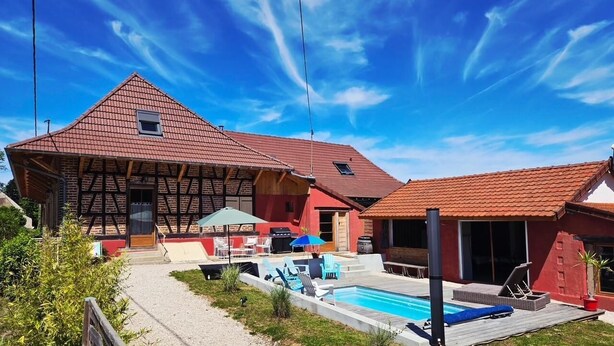 Una casa de dos pisos con techo de tejas rojas, piscina y un patio con mobiliario exterior.