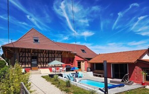 Ein zweigeschossiges Haus mit rotem Ziegeldach, einem Swimmingpool und einer Terrasse mit Gartenmöbeln.