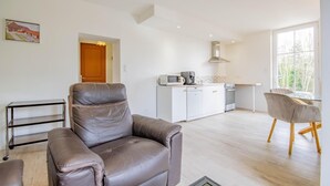 Una sala de estar moderna con un sofá de cuero, una zona de comedor con una mesa de vidrio y una cocina con gabinetes y electrodomésticos blancos.
