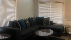 A living room with a sectional sofa, two side tables, and a large window with blinds. - Charming 2bedroom house with WiFi, AC in peaceful Indianapolis. Quiet cul-de-sac (Indianapolis)