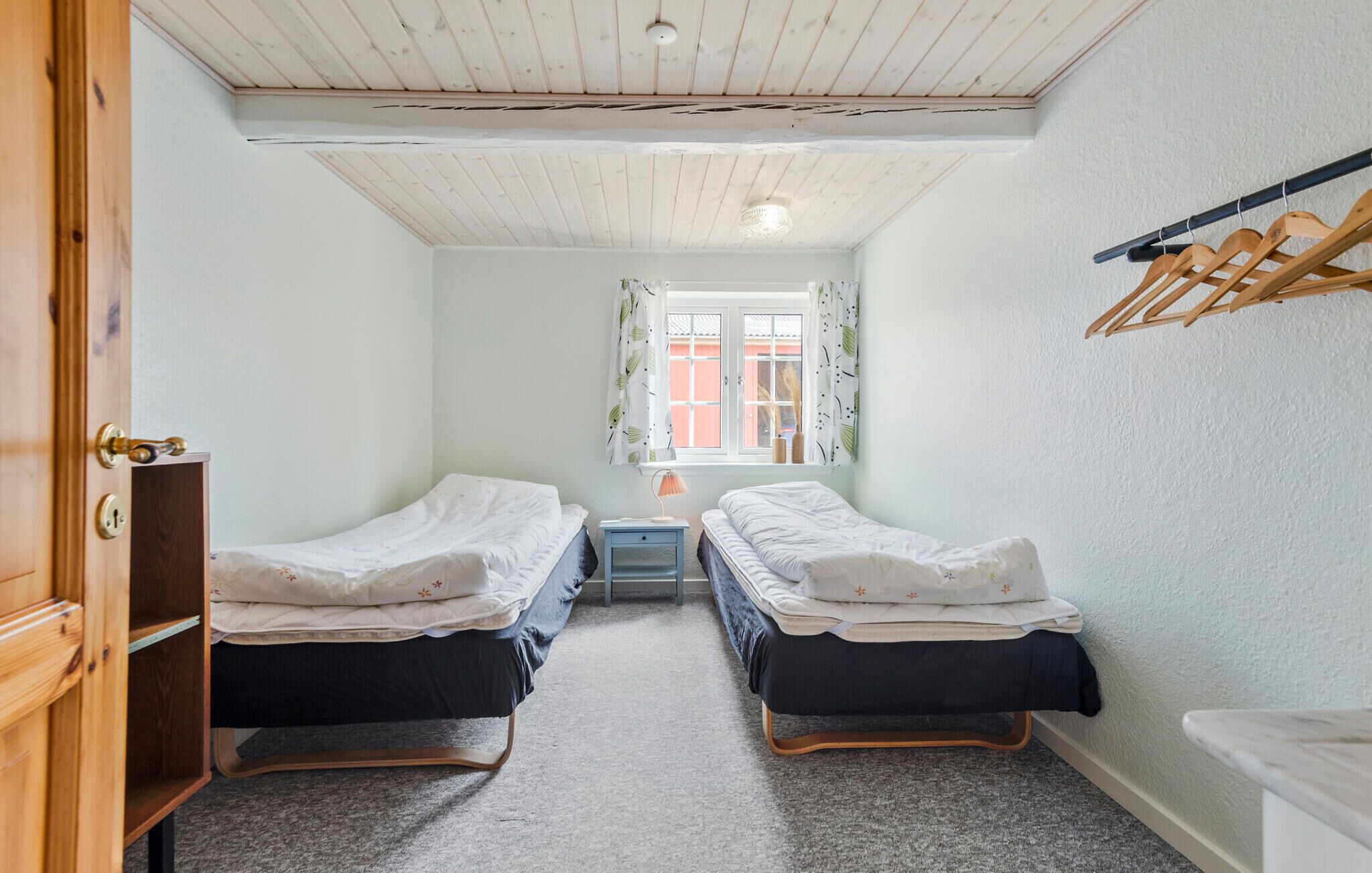 Una camera da letto piccola e luminosa con due letti singoli, un tavolino, una finestra con tende e un armadio in legno.