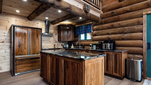 Cocina de cabaña de troncos con armarios de madera, una isla central y un cubo de basura de acero inoxidable.