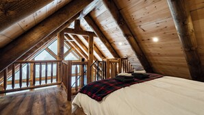 Una habitación de madera con techos altos, una cama, un ventanal y un balcón.