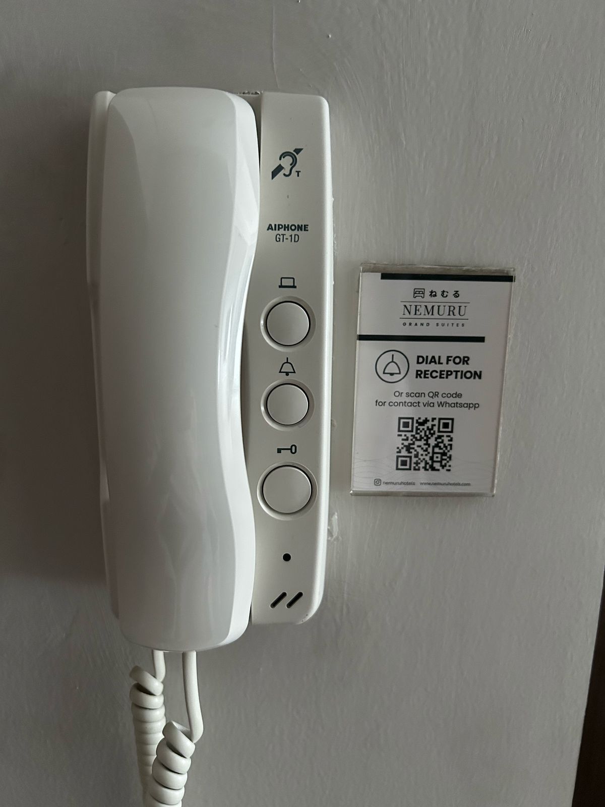 A white hotel phone with a QR code for contact via WhatsApp.
