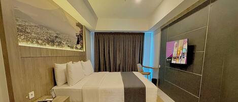 A modern hotel room with a large bed, a flat-screen TV, a sofa, and a wall-mounted TV.