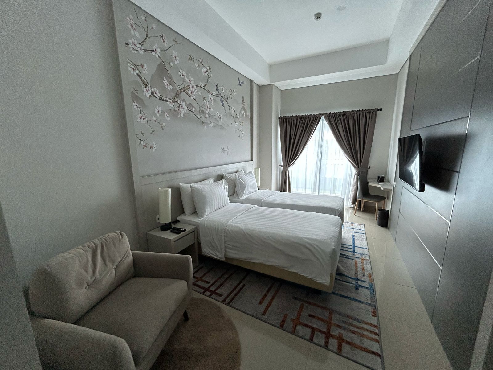 A modern hotel room with a large bed, a sofa, a TV, and a decorative wall mural.