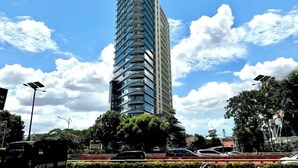 Un grand immeuble moderne à la façade incurvée, entouré d’arbres et de voitures garées.