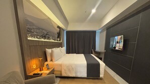 Une chambre d’hôtel moderne équipée d’un grand lit, d’un bureau, d’une chaise et d’un téléviseur fixé au mur.