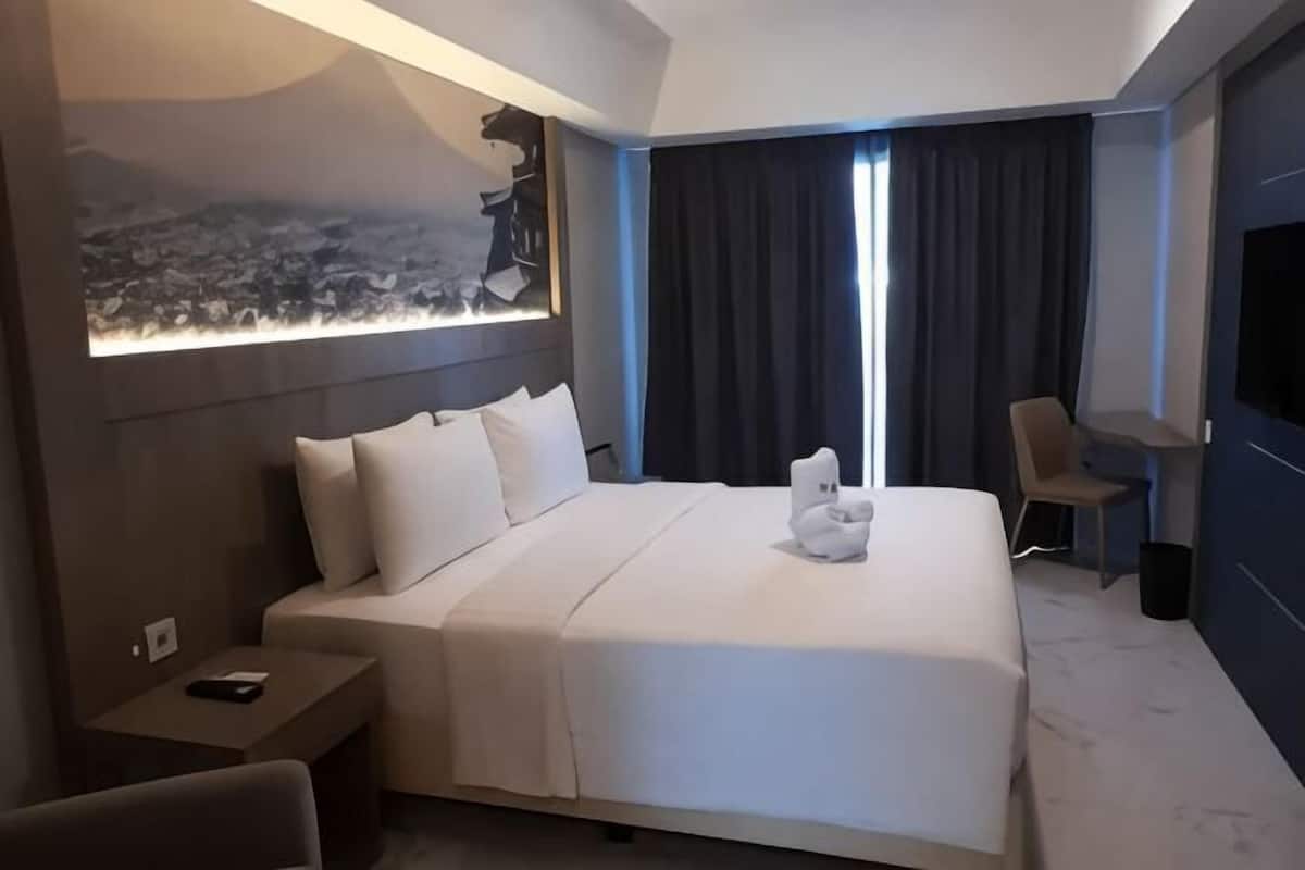 A hotel room with a large bed, a desk, a chair, a TV, and a view of the city through the window.