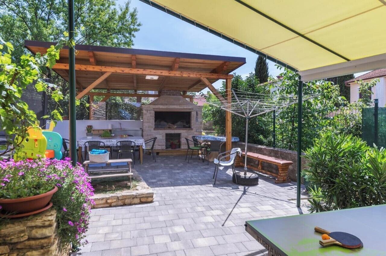 An outdoor patio with a brick floor, wooden pergola, and a barbecue area.