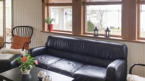 A room with a black leather sofa, a wooden chair with a cushion, a small table with a vase of flowers, and a window with blinds and two lanterns. - Awesome home in Lekeryd with WiFi (Lekeryd)