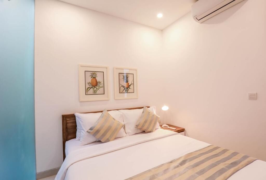 Une chambre à coucher avec un lit, deux tableaux encadrés au mur, une table de chevet avec une lampe et un appareil de climatisation.