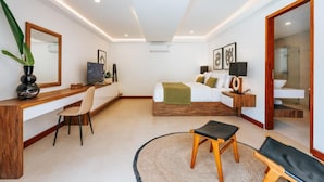 Une chambre d’hôtel moderne avec un bureau en bois, un lit recouvert d’un plaid vert, un grand miroir et une vue sur la salle de bain.