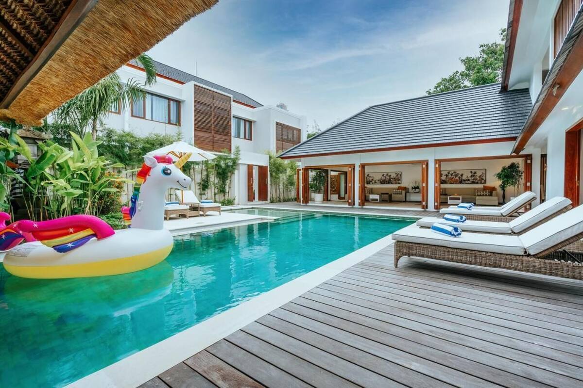 A modern house with a swimming pool, a wooden deck, and a lounge area with sun loungers.
