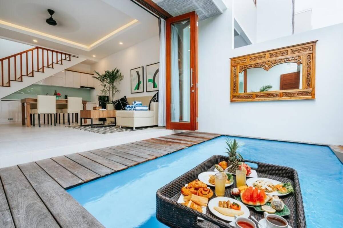 A modern living area with a pool, dining setup, and a staircase leading to a kitchen.