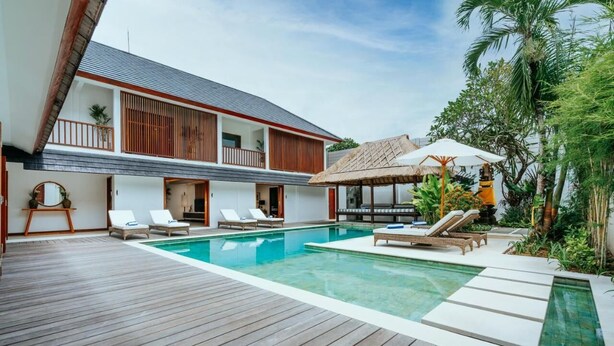 Une villa moderne dotée d’une terrasse en bois, d’une piscine et de chaises longues.
