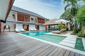 Une villa moderne dotée d’une terrasse en bois, d’une piscine et de chaises longues.