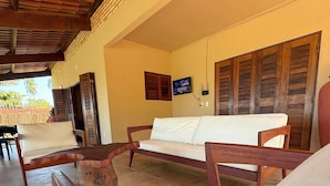 Una habitación con techo de madera, un sofá blanco, una silla de madera y un televisor en la pared.
