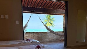 Una habitación con dos camas, una hamaca y vista a la playa y una palmera.