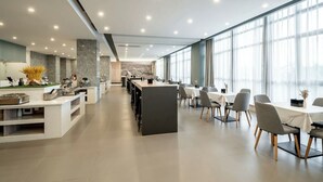 Moderni hotellin aula, jossa on keskeisellä paikalla sijaitseva baaritiski, ruokapöytiä ja suuret ikkunat, joista tulee runsaasti luonnonvaloa.
