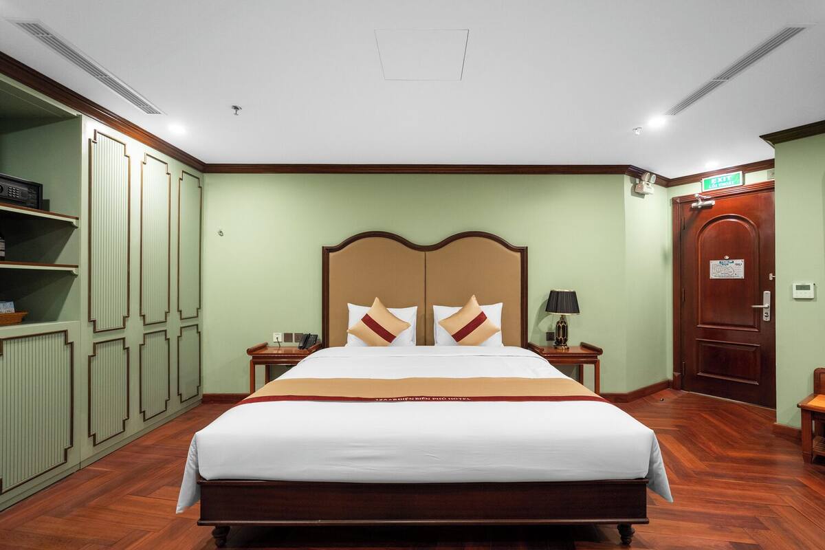 Habitación de hotel con una cama grande, una mesita de noche, una lámpara, un armario y una puerta de salida.