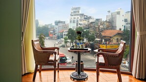 A room with two wooden chairs and a small table with a vase, a view of a cityscape through a window with curtains.