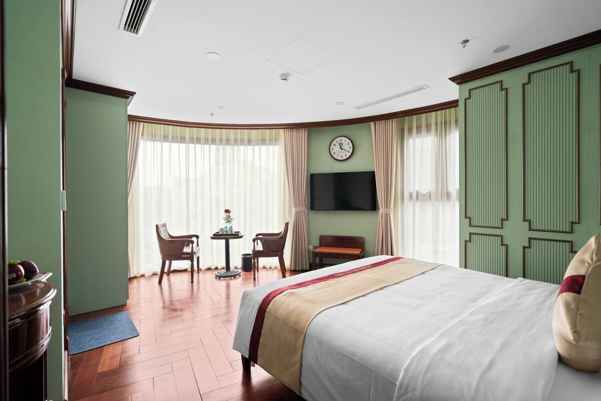 Habitación de hotel con cama, escritorio, silla, televisor y un reloj en la pared.