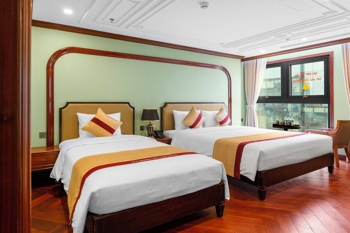Habitación de hotel con dos camas, piso de madera, un ventanal grande con cortinas y vista a la ciudad.