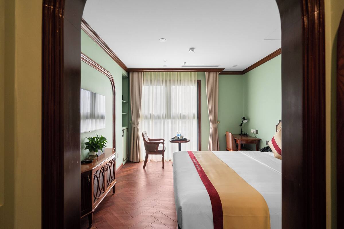 Habitación de hotel con una cama grande, un escritorio, una silla, una mesita y una planta en maceta.
