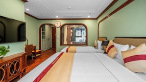 A hotel room with a large bed, a TV, a wooden cabinet, and a view of the street through a window.