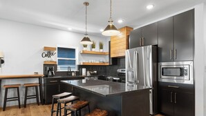A modern kitchen with a central island, stainless steel appliances, and wooden bar stools.