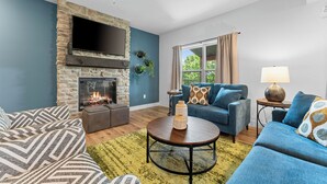 A living room with a stone fireplace, blue walls, and a large window with curtains.