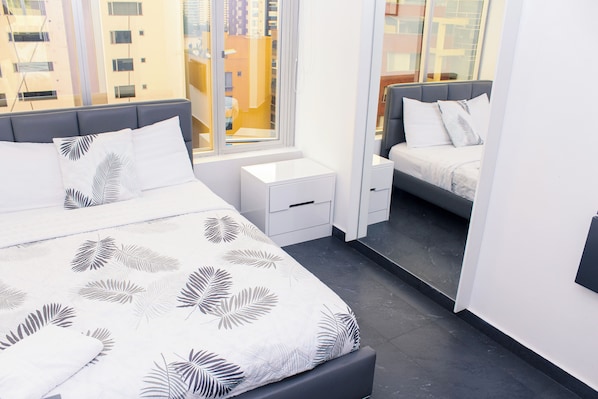 A modern bedroom with a large bed, a smaller bed, a nightstand, and a wardrobe.