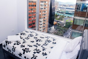 A hotel room with a bed, a window, and a view of a cityscape.