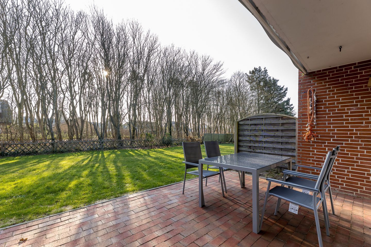An outdoor patio with a table and chairs, a brick floor, and a view of a grassy area with trees.