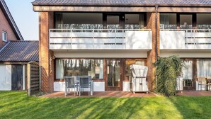 Ein zweistöckiges Haus mit Balkon, Terrasse und Gartenmöbeln sowie einem gepflegten Rasen.