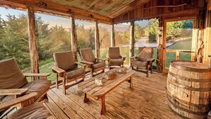 A covered outdoor seating area with wooden furniture and a barrel. - Cabin on Private 4-Acre Pond, King Bed (Junction City)
